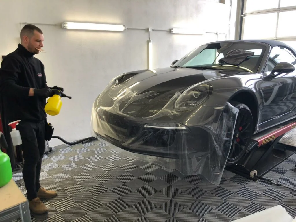 Auf der Front Seite eines schwarzen Porsches wird eine Folierung aufgetragen.